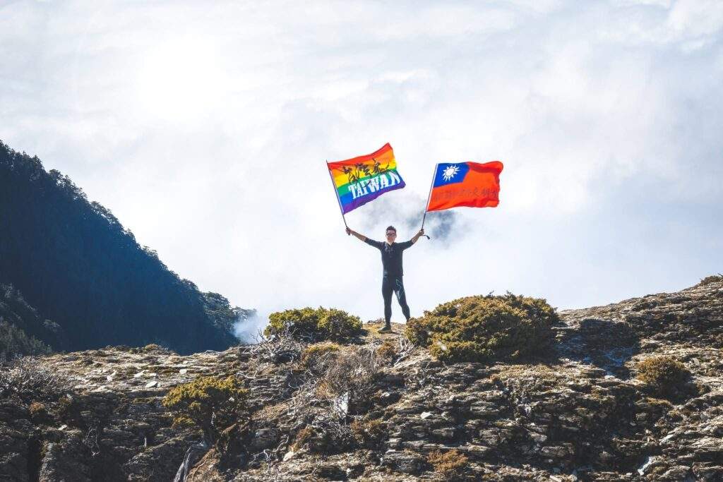 一位登山者在百岳巔峰揮舞旗幟，象徵透過時序調整策略，在熱門路線中成功避開人潮，享受高山獨行體驗的珍貴瞬間。