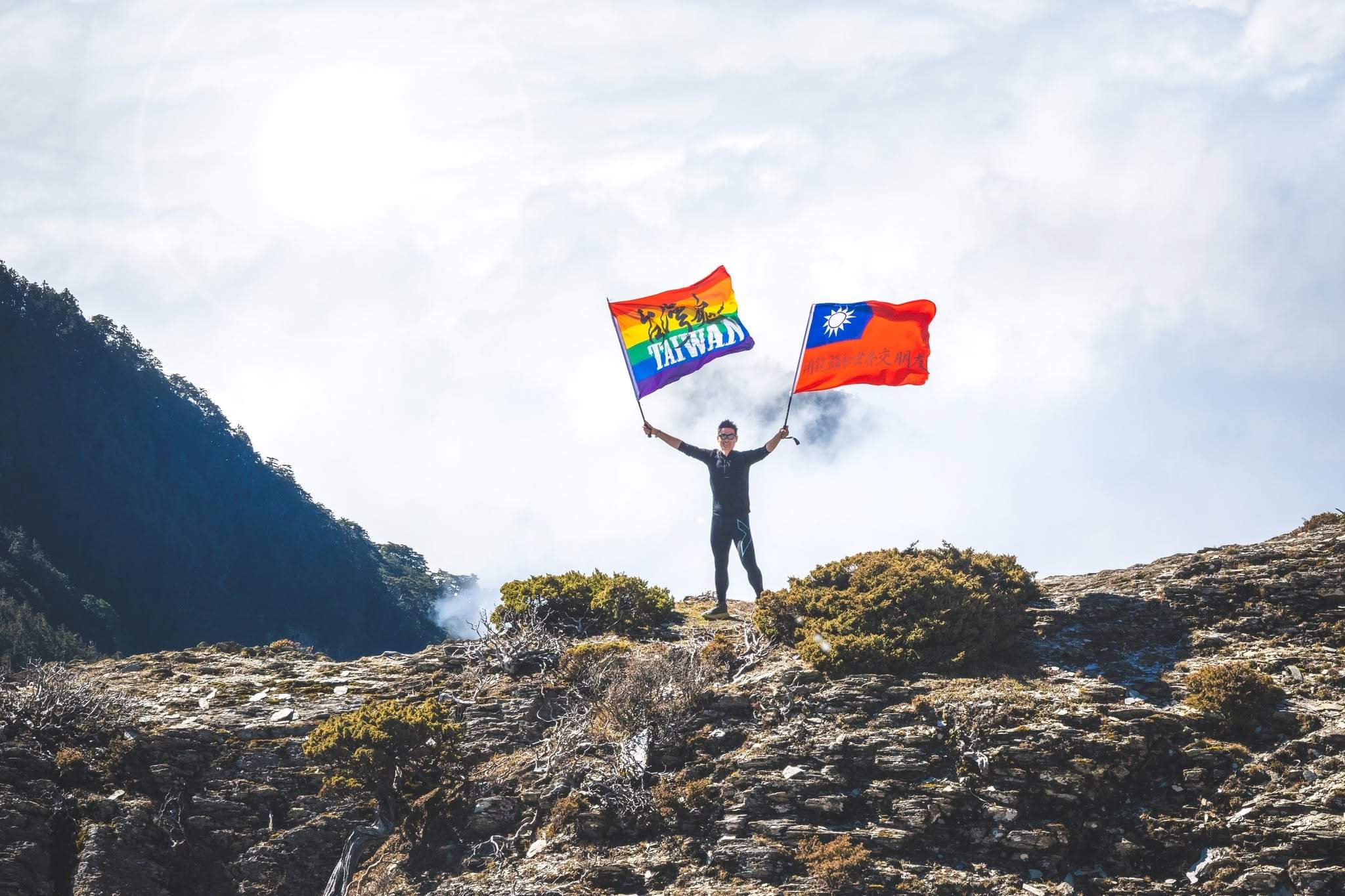 一位登山者在百岳巔峰揮舞旗幟,象徵透過時序調整策略,在熱門路線中成功避開人潮,享受高山獨行體驗的珍貴瞬間。